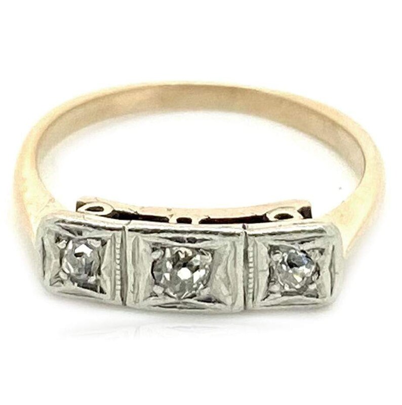 May include: A gold band ring with three square-shaped settings, each containing a small round diamond. The ring is made of both yellow and white gold.