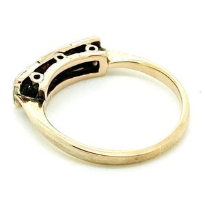 May include: A gold band ring with a row of three small round stones set in a black metal frame.