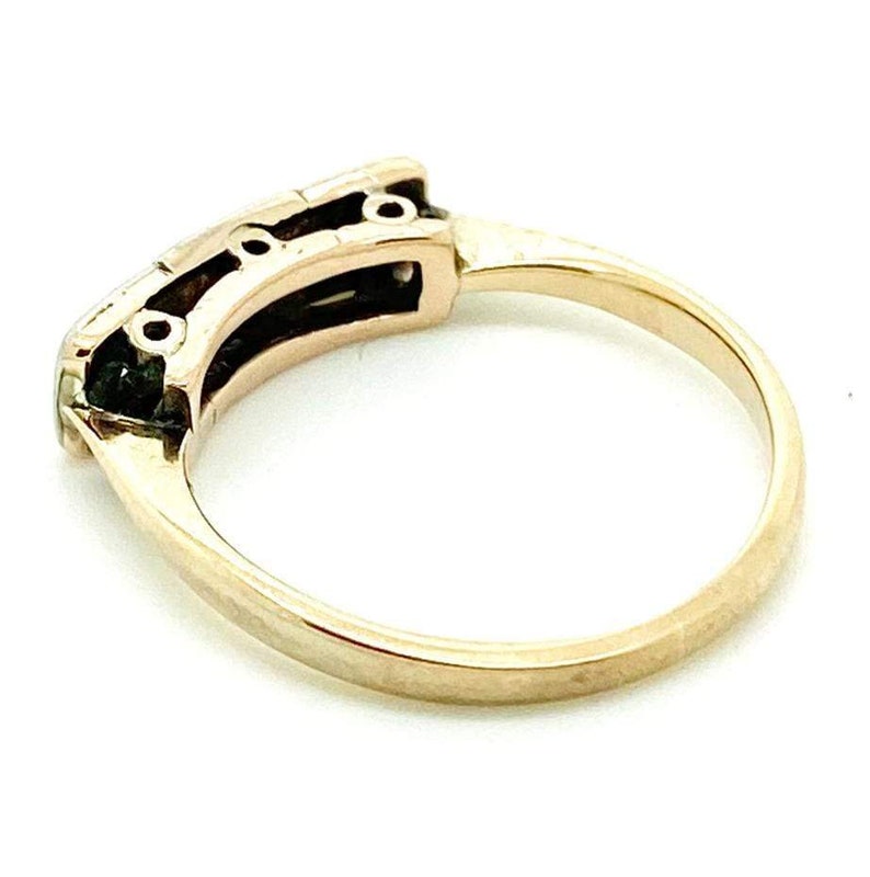 May include: A gold band ring with a row of three small round stones set in a black metal frame.
