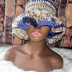 May include: A crocheted bucket hat with a brown, blue, and white color scheme. The hat has a wide brim and a ruffled edge.
