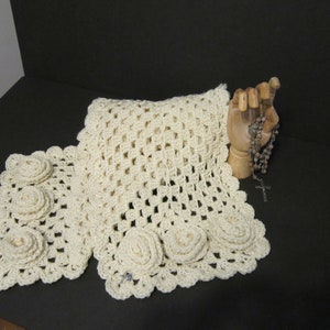 May include: A crocheted scarf with a cream color and a floral design. The scarf has three large crocheted flowers on each end.