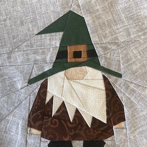 Könnte beinhalten: Ein brauner und weißer Zwerg mit einem grünen Hut und einem braunen Gürtel. Der Zwerg ist aus Stoff und ist ein Patchwork-Design.