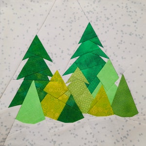 Può includere: Un blocco di tessuto con un design patchwork di alberi sempreverdi in varie tonalità di verde e verde-giallo. Gli alberi sono ambientati su uno sfondo bianco con un sottile motivo di piccoli punti grigi, creando una scena invernale.