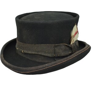 May include: A black top hat with a distressed look and a brown ribbon. A small white feather with red accents is attached to the side of the hat.