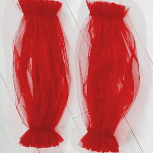 May include: A pair of red tulle sleeves with ruffled edges. The sleeves are sheer and flowy.