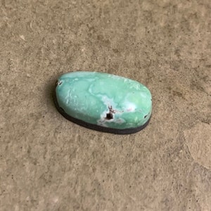 May include: A light green oval cabochon gemstone with brown and black inclusions. The stone is set in a silver bezel.