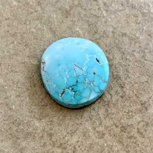 May include: A light blue oval-shaped turquoise cabochon with a marbled pattern and white veins.