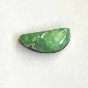 May include: A green cabochon gemstone with white flecks and a dark brown edge.