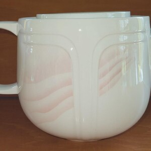 Peut inclure: Une théière en céramique blanche avec un corps arrondi, une anse incurvée et un bec verseur. La théière présente un motif de vagues roses subtiles sur les côtés. Le couvercle est plat et rectangulaire. Pour le service du thé.