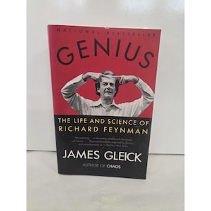 May include: A book titled Genius: The Life and Science of Richard Feynman by James Gleick. The cover features a black and white photograph of Richard Feynman gesturing with his hands against a red background, with black text at the bottom.