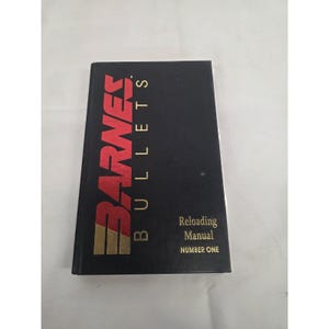 May include: A black hardcover book titled Barnes Bullets Reloading Manual Number One. The front cover features the word Barnes in large red and gold lettering, with the word Bullets and the subtitle printed in gold text on the black background.