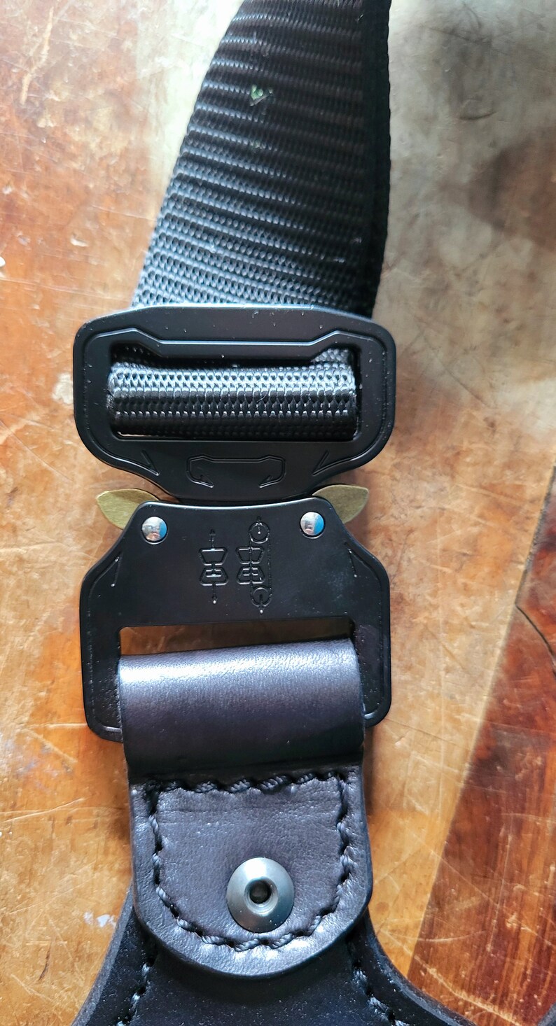 May include: Black and silver adjustable buckle with a black nylon strap and a black leather strap with a stitched edge. The buckle has a brass slider and the text "COBRA" is printed on the buckle.