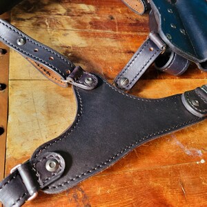 May include: A black leather holster with adjustable straps for carrying a firearm. The holster has a smooth, polished finish and is designed for concealed carry.
