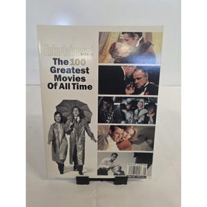 May include: Entertainment Weekly magazine titled The 100 Greatest Movies Of All Time. The cover features a large black and white photo of two people walking with an umbrella, alongside a column of smaller film stills from various movies.