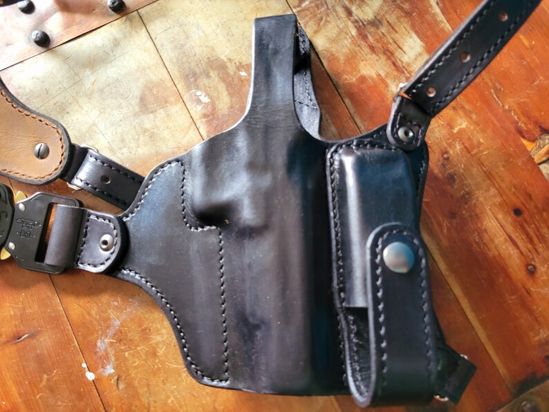 May include: Black leather shoulder holster with a magazine pouch. The holster has a stitched design and a snap closure.