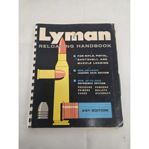 Könnte beinhalten: Das Lyman Reloading Handbook 44th Edition ist ein spiralgebundenes Handbuch mit schwarzem Einband und einer gelben Grafik einer Patrone und eines Geschosses. Der Text enthält Daten für Gewehr, Pistole, Schrotflinte und Vorderlader.