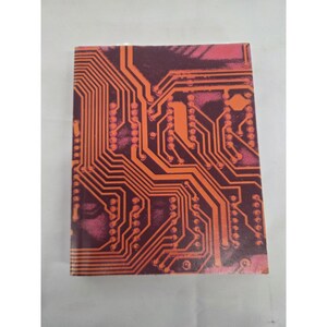 May include: A rectangular notebook with a hard cover featuring a vibrant orange circuit board pattern printed over a dark purple and magenta background. The design consists of intricate lines and circular nodes that mimic electronic pathways.