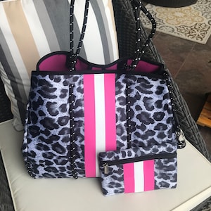 May include: A gray and white leopard print tote bag with a pink and white stripe down the center. The bag has a black zipper and a matching smaller pouch.