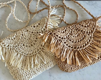 May include: Two straw handbags with fringe detailing. The handbag on the left is white and the handbag on the right is brown.