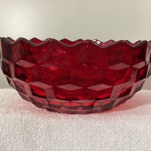 May include: A ruby red glass bowl with a geometric diamond pattern. The bowl has a scalloped rim and is made of transparent glass. The bowl is sitting on a white surface.