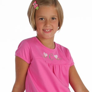 May include: A pink short-sleeved top with a white heart and letter G embroidery. The top is paired with a green and pink floral print skirt.