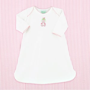 Könnte beinhalten: Weißes Langarmkleid mit rosa Besatz und einem gestickten rosa Hasen mit grüner Schleife auf der Vorderseite. Das Kleid trägt den Text "littles" in grün auf der Vorderseite.