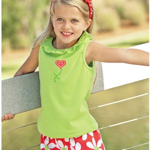 Puede incluir: Una niña pequeña con una camiseta verde sin mangas con un bordado de flor de corazón rojo y una falda de estampado de margarita roja y blanca.