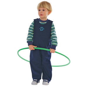 May include: A young child wearing blue overalls with a green and blue striped shirt. The overalls have a blue embroidered letter 'D' on the front. The child is holding a green hula hoop.