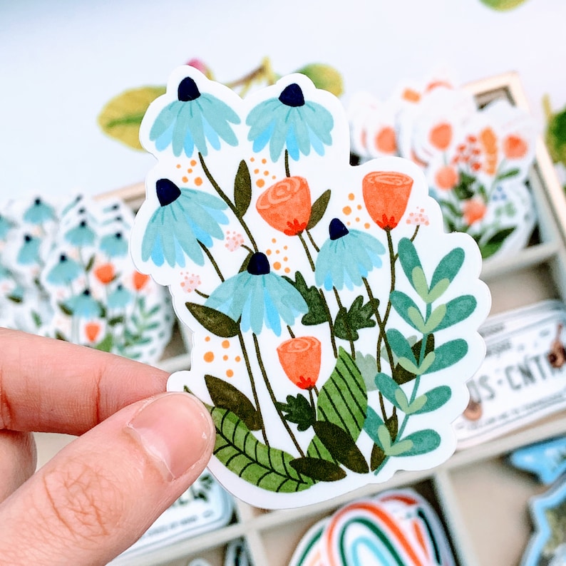 May include: A sticker featuring a cluster of blue and orange flowers with green leaves. The flowers are stylized and have a whimsical feel.