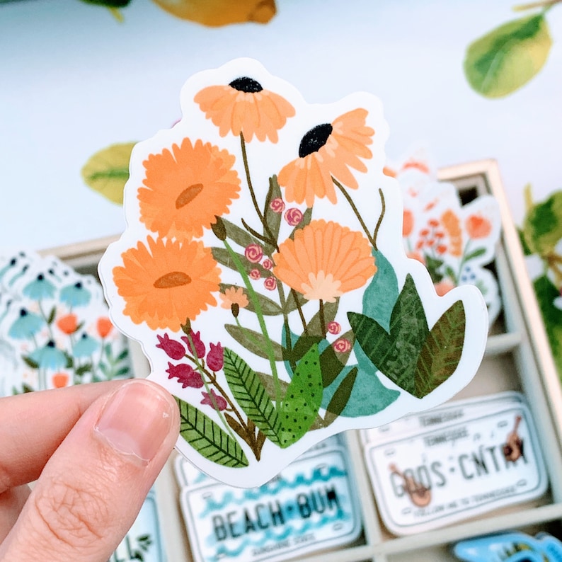 May include: A sticker featuring a cluster of orange and yellow flowers with green leaves. The flowers have a watercolor-like appearance and are arranged in a bouquet-like shape.