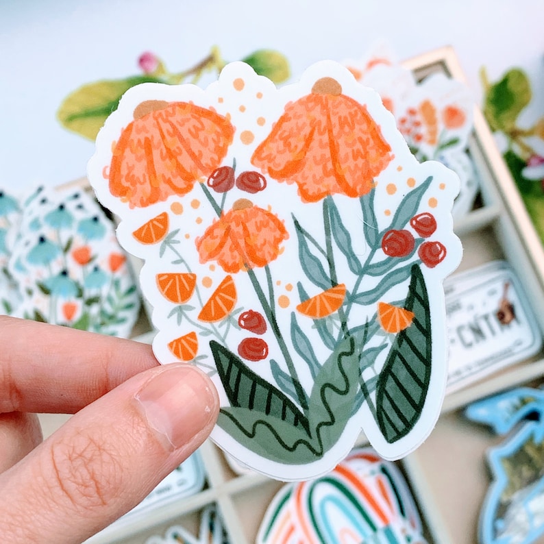 May include: A sticker featuring a floral design with orange flowers and green leaves. The flowers are stylized and have a textured appearance. The sticker is on a white background.