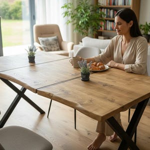 May include: A wooden dining table with a natural edge and black metal legs. The table is set with small potted plants. The table is approximately 183 cm long and 91 cm wide. Two grey chairs are positioned near the table.