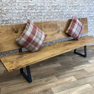May include: A long wooden bench with a backrest and black metal legs. The bench is decorated with two red and white plaid pillows.