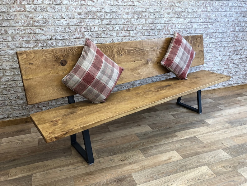 May include: A long wooden bench with a backrest and black metal legs. The bench is decorated with two red and white plaid pillows.
