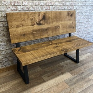 May include: A wooden bench with a backrest and black metal legs. The bench is made of reclaimed wood and has a rustic finish.