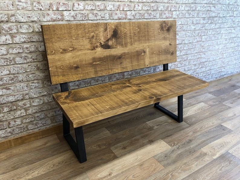 May include: A wooden bench with a backrest and black metal legs. The bench is made of reclaimed wood and has a rustic finish.