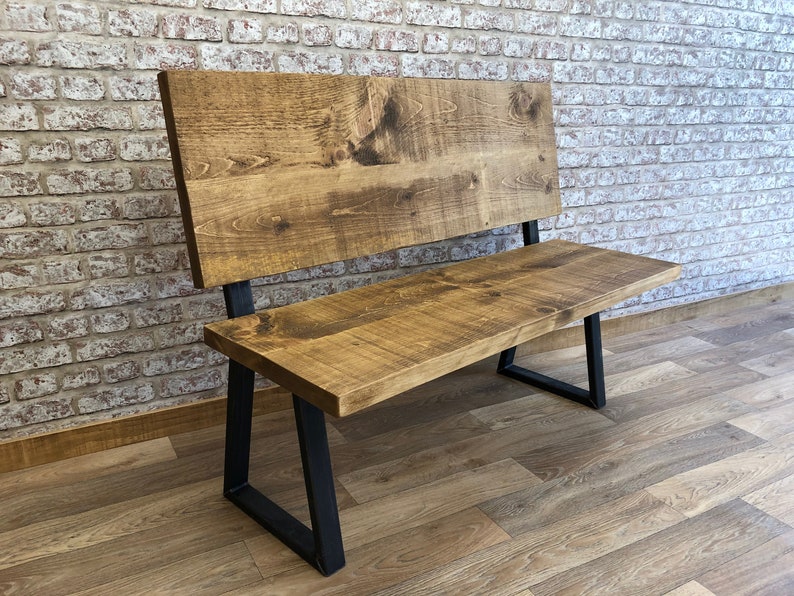 May include: A wooden bench with a backrest and black metal legs. The bench is made of reclaimed wood and has a rustic finish.