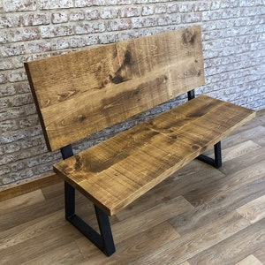 May include: A wooden bench with a backrest and black metal legs. The bench is made of reclaimed wood and has a rustic finish.