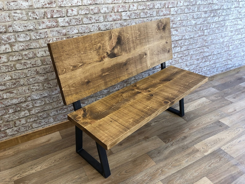 May include: A wooden bench with a backrest and black metal legs. The bench is made of reclaimed wood and has a rustic finish.