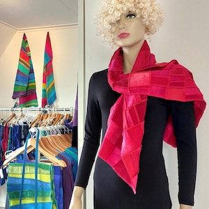 Könnte beinhalten: Ein leuchtend pinker Schal mit einem Patchwork-Design aus verschiedenen Rosa- und Rottönen. Der Schal liegt um den Hals einer Schaufensterpuppe, die ein langärmeliges schwarzes Oberteil trägt. Der Stoff weist eine sichtbare Textur und Glanz auf.