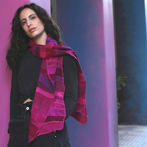 May include: A woman wearing a black shirt and jeans with a pink and purple patterned scarf around her neck.