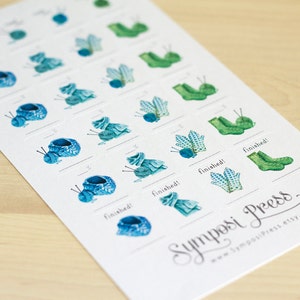 Könnte beinhalten: Eine weiße Karte mit einem blauen und grünen Strick-Sticker-Chart. Das Chart hat 15 Reihen mit Stickern, die verschiedene Phasen von Strickprojekten zeigen. Die Sticker zeigen eine Mütze, Fäustlinge und Socken. Die Karte hat den Text "fertig!" und den Text "Symposi Press" unten.