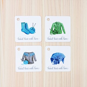 Könnte beinhalten: Vier weiße Geschenkanhänger mit handgezeichneten Illustrationen von gestrickten Artikeln. Jeder Anhänger zeigt ein anderes Objekt: ein Paar blaue Socken, einen grünen Pullover, einen grauen Pullover und einen blauen Schal. Jeder Anhänger trägt den Text "hand knit with love" in Kursivschrift.