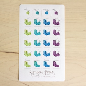 Pode incluir: Uma folha de 20 adesivos coloridos com ilustrações de agulhas de tricô e novelos de lã. Os adesivos são projetados para acompanhar projetos de tricô com o texto "cast on!" e "finished!" nos adesivos.