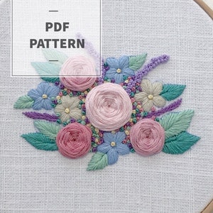 Puede incluir: Un bordado a mano en un bastidor con un diseño floral. El diseño incluye rosas rosas, flores azules y beige, y hojas verdes. El texto "PDF PATTERN" se muestra en un cuadro blanco.