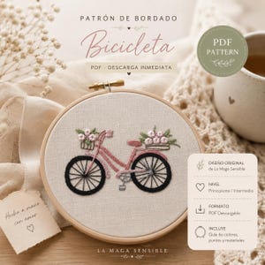 May include: An embroidery hoop featuring a pink bicycle design with flower baskets, stitched on a beige fabric. The text "Bicicleta" is above the bicycle. The design includes the text "PDF Pattern" and "PDF Descarga Inmediata".