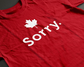 Pode incluir: Camiseta vermelha com uma folha de bordo branca e o texto "Desculpe." impresso na frente.