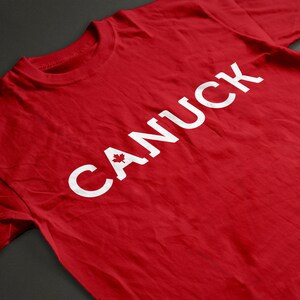 May include: Red t-shirt with the word "CANUCK" printed in white with a Canadian maple leaf in the "C".