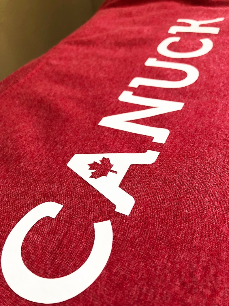 May include: Red t-shirt with white text that reads "CANUCK" with a Canadian maple leaf in the "A".
