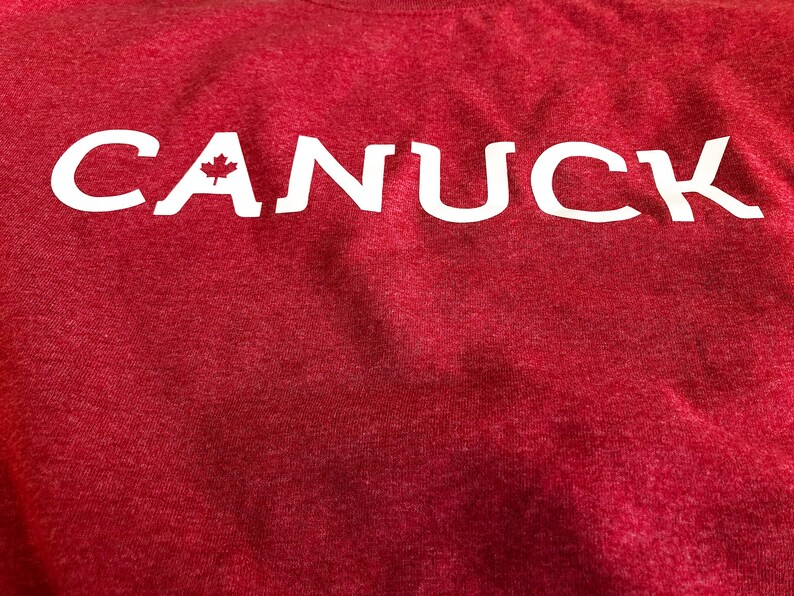 May include: Red t-shirt with white lettering that says "CANUCK" with a small Canadian maple leaf in the "A".